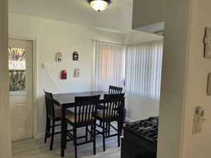Un coin repas avec une table et des chaises, une fenêtre avec des stores et une cuisinière.
