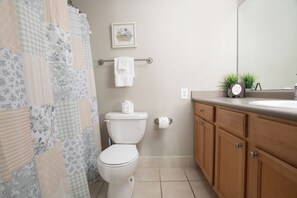 A bathroom with a toilet, a sink, wooden cabinets, a towel rack, and a framed picture on the wall.