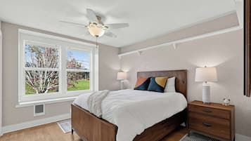 A bedroom with a bed, bedside tables, a ceiling fan, and a window with a view of trees.