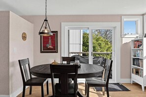 A dining area with a round table, four chairs, a pendant light, a framed picture, a sliding glass door leading to a balcony, and a bookshelf. - Riverlight - Nehalem Riverfront for 2 (Nehalem)