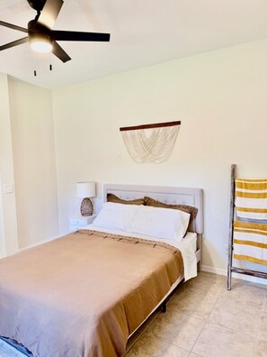 Een slaapkamer met een bed, een plafondventilator, een wandlamp en een handdoekhouder.