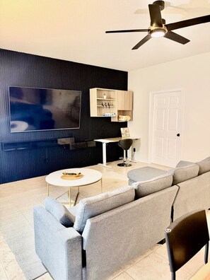 Een moderne woonkamer met een flatscreen televisie, een plafondventilator, een bank, een salontafel en een klein kastje.