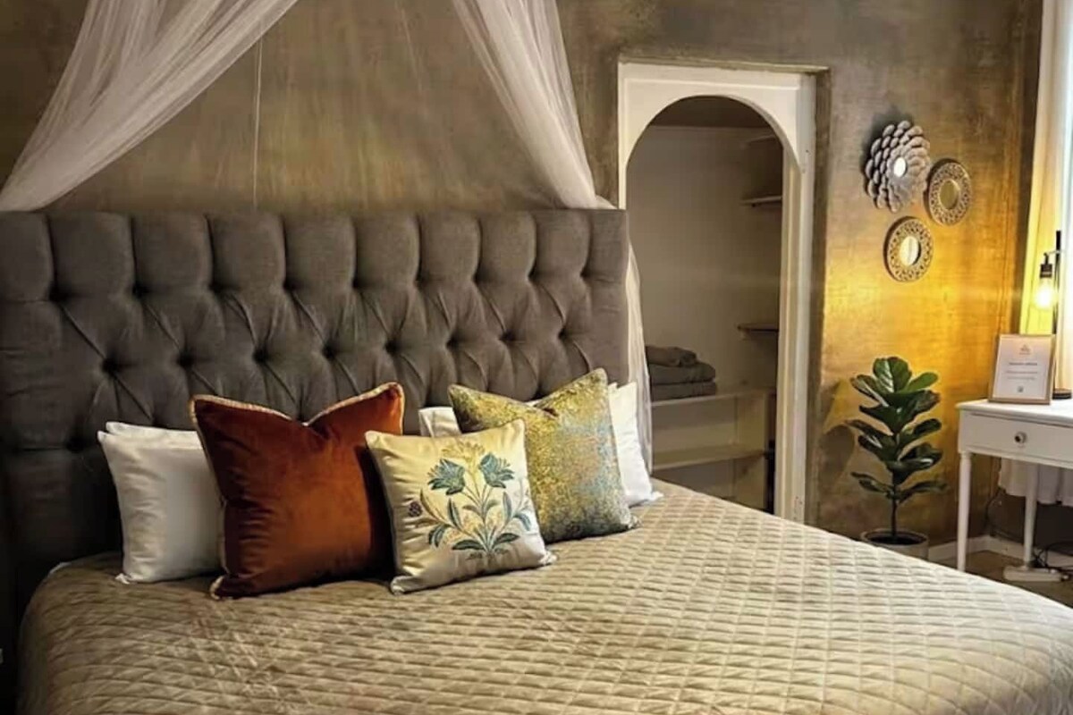 A bed with a tufted headboard, multiple pillows, and a canopy.