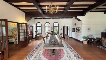A spacious room with a long wooden table, a patterned rug, and a chandelier.