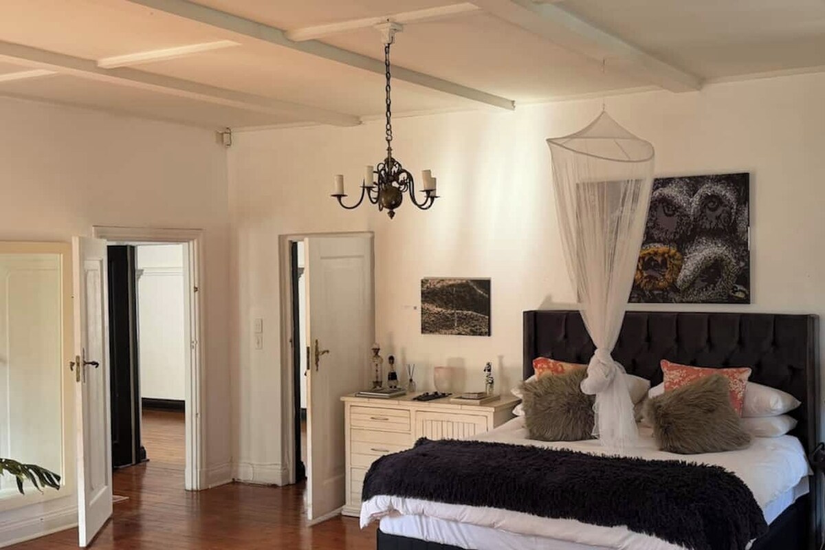 A bedroom with a bed, a bedside table, a nightstand, a chandelier, and artwork on the walls.