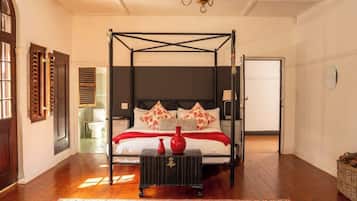 A four-poster bed with a dark headboard, a red vase on a side table, and a patterned rug on the floor.