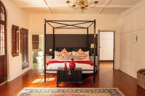 A four-poster bed with a dark headboard, a red vase on a side table, and a patterned rug on the floor. - Glenhof Manor (Cape Town)