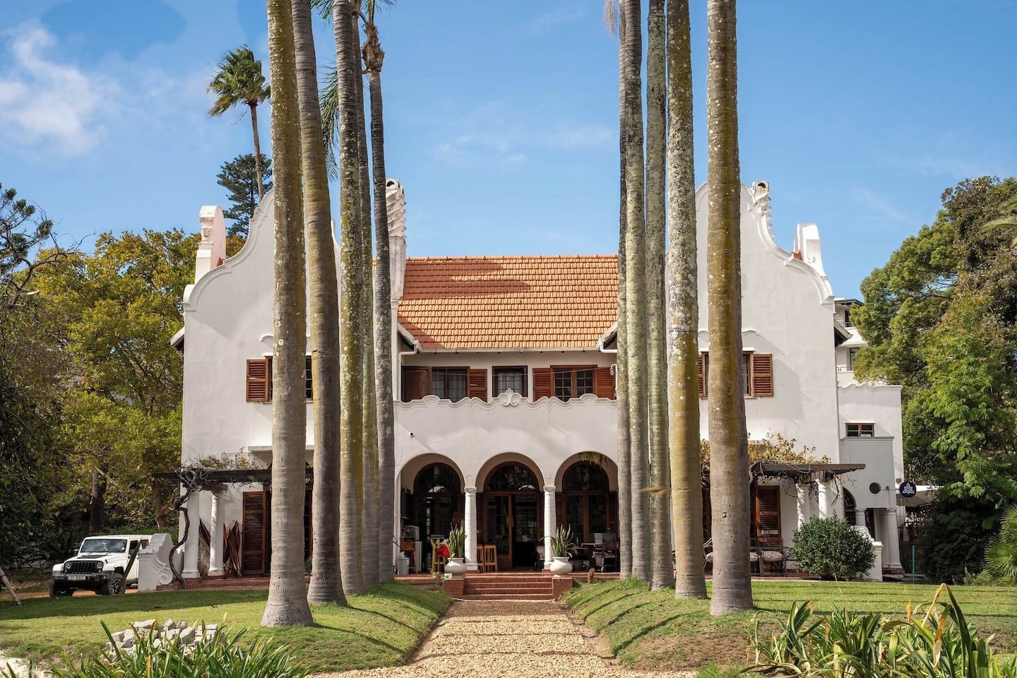 A large, white building with a tiled roof, surrounded by tall palm trees.