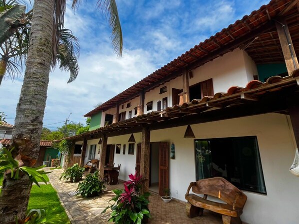 A two-story building with a tiled roof, a covered patio area, and a garden with palm trees and potted plants.