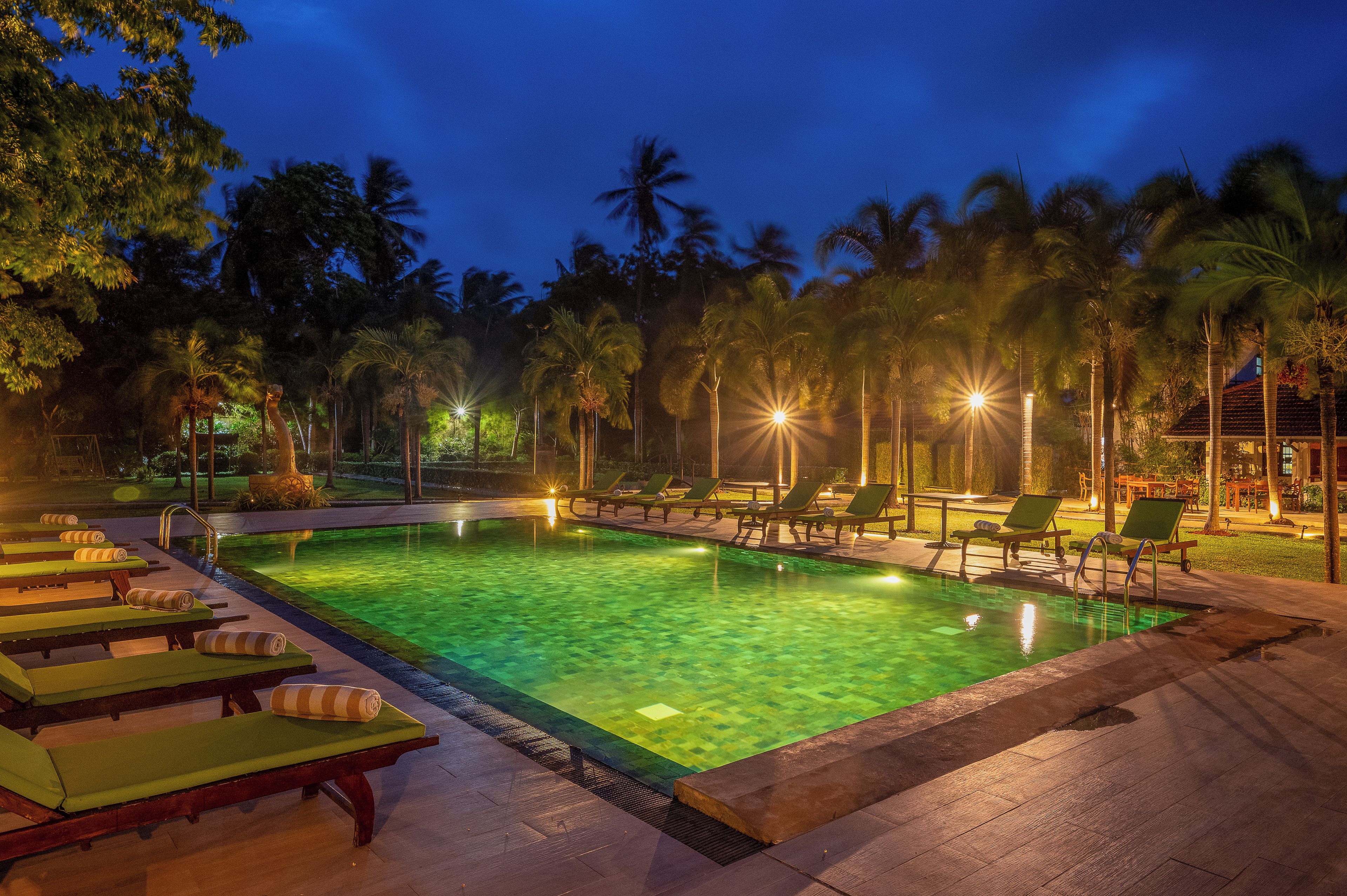 Zona de piscina con sillones de descanso y palmeras al anochecer.