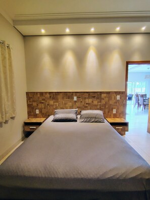 Une chambre moderne avec un grand lit, une tête de lit en bois, des tables de chevet et une vue sur l’espace extérieur aménagé pour se détendre.