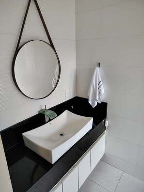 Une salle de bain moderne avec un lavabo blanc, un plan de toilette noir et un miroir rond.