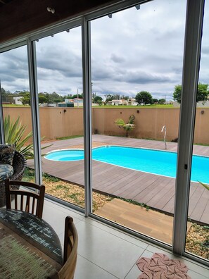 On peut apercevoir, à travers de grandes portes vitrées, un espace piscine avec une terrasse et une chaise.