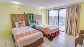 Habitación de hotel con dos camas, un escritorio pequeño, una silla y un balcón con vistas.