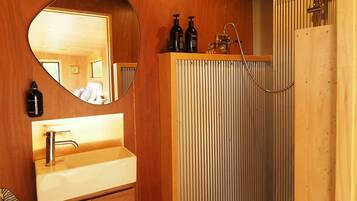 Un baño con tocador de madera, un espejo redondo, ducha con puerta de cristal y una toalla colgada en la pared.
