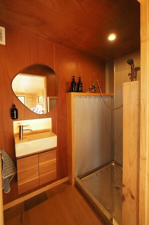 A bathroom with a wooden vanity, a round mirror, a shower with a glass door, and a towel hanging on the wall.