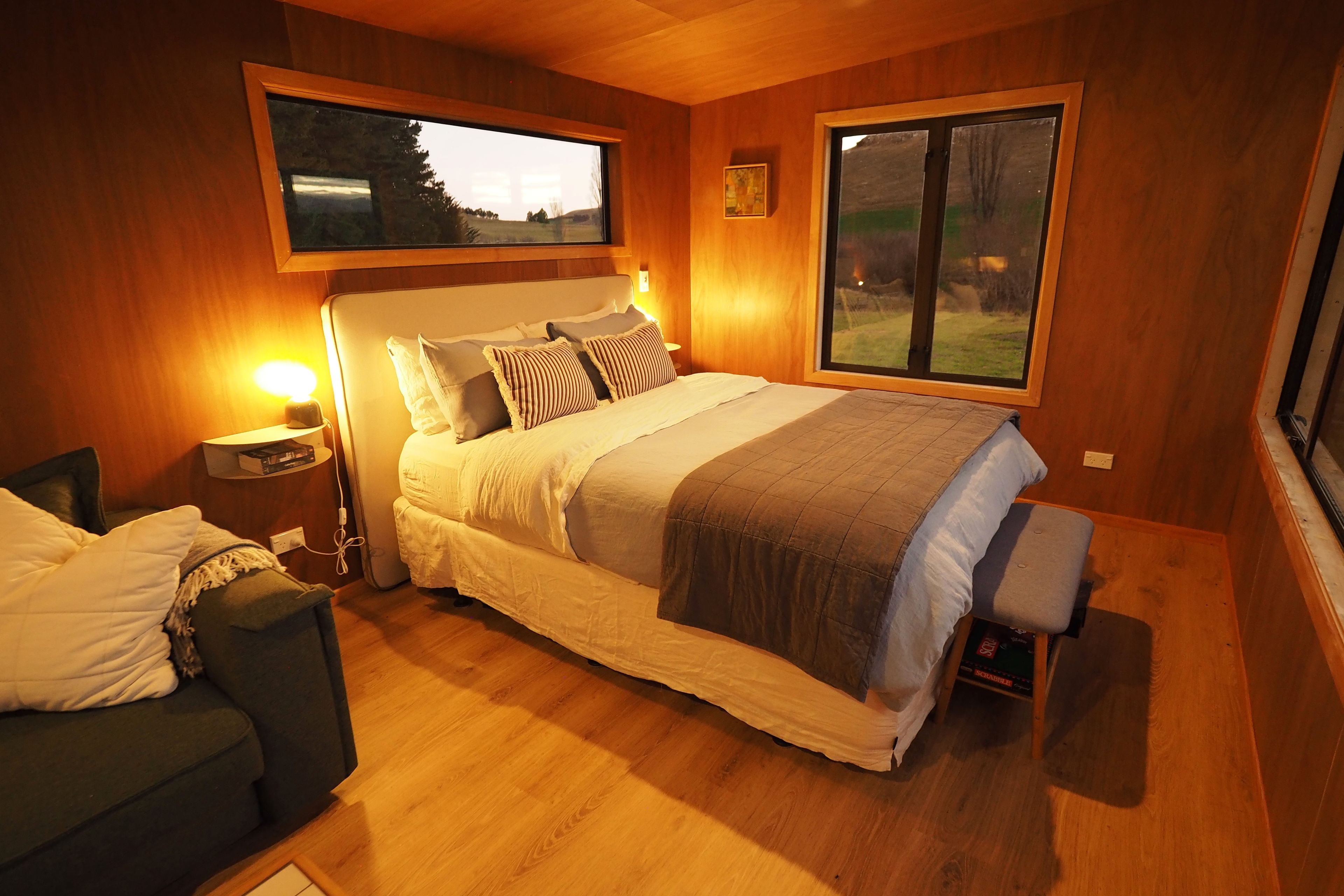 Un dormitorio con cama, mesitas de noche, una silla y una ventana con vistas.