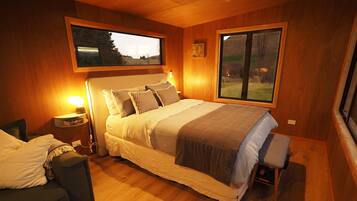 Un dormitorio con cama, mesitas de noche, una silla y una ventana con vistas.