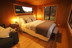 A bedroom with a bed, bedside tables, a chair, and a window with a view.