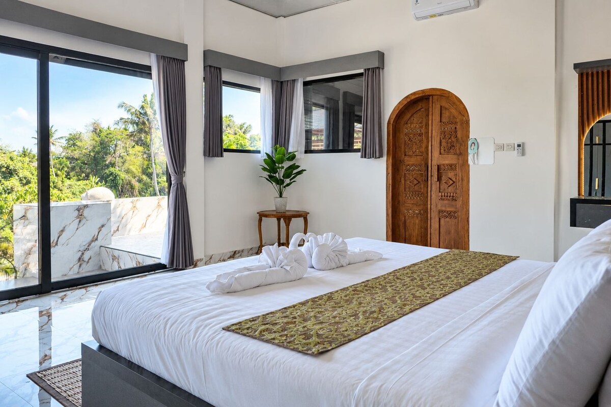 Ein Hotelzimmer mit einem großen Bett, einer Holztür und Blick auf Palmen.