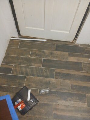 A room with a wooden floor, a closed white door, and a black object on the floor.