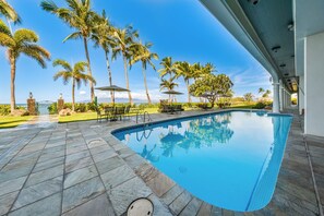 Une piscine dotée d’une plage en pierre, entourée de palmiers et agrémentée de mobilier d’extérieur.