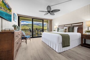 Une chambre avec un grand lit, un ventilateur de plafond, une vue sur l’extérieur et un balcon avec des chaises.