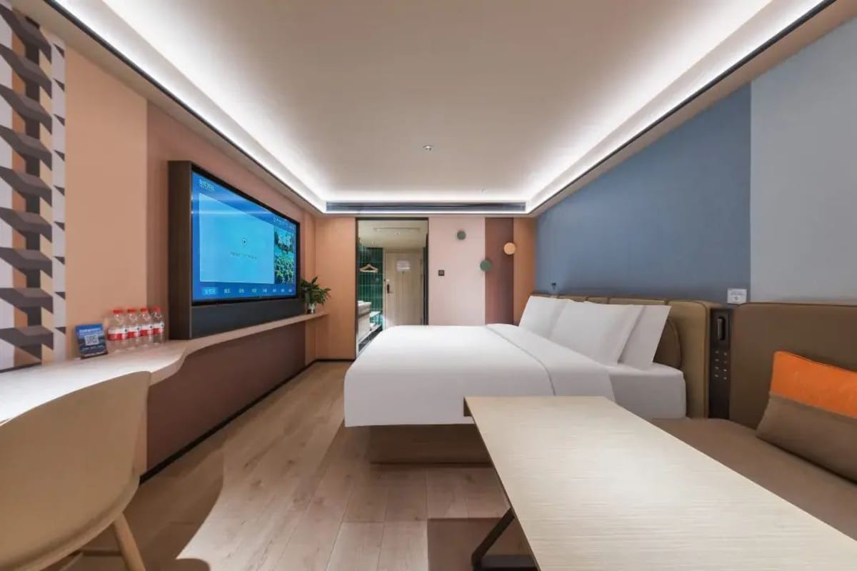 Una habitación de hotel moderna con una cama, un escritorio con monitor de computadora y una zona de estar.