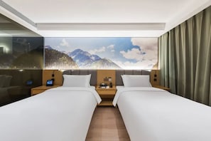Habitación de hotel con dos camas, un ventanal con vista a la montaña, una mesita de noche con lámpara y un televisor montado en la pared.