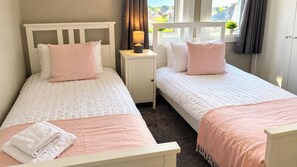 Een slaapkamer met twee eenpersoonsbedden, een nachtkastje met een lamp en een raam met gordijnen.