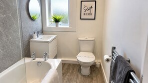 Een moderne badkamer met bad, wastafel en toilet.