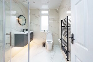 Ein modernes Badezimmer mit einer Duschkabine aus Glas, einer weißen Toilette, einem schwarzen Handtuchhalter und einem Boden mit Marmorfliesen.