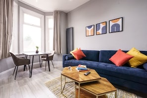 Ein modernes Wohnzimmer mit einem blauen Sofa, einem Holztisch und einem Essbereich mit Tisch und Stühlen.