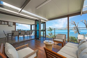A spacious indoor area with a wooden floor, a dining table with chairs, and a seating area with a view of a lake. - Spacious 4-bedroom house in peaceful Taren Point with AC (Taren Point)