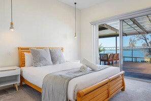 A bedroom with a bed, bedside tables, and a view of the outdoors through a sliding glass door. - Spacious 4-bedroom house in peaceful Taren Point with AC (Taren Point)