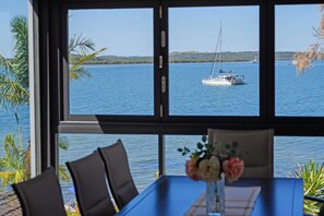 A dining area with a view of a calm sea and a sailboat. - Spacious 4-bedroom house in peaceful Taren Point with AC (Taren Point)