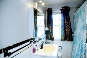 Une salle de bain avec un lavabo blanc, un miroir, une fenêtre avec des rideaux à motifs et un porte-serviettes.
