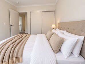 A hotel room with a bed, a bedside lamp, and a door leading to a bathroom. - Slow Days on Wellington | A Family Retreat (Yarrabilba)