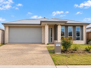 A single-story residential building with a garage, a front porch, and a small garden area. - Slow Days on Wellington | A Family Retreat (Yarrabilba)