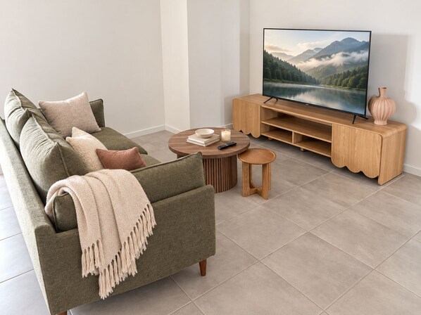 A modern living room with a green sofa, a wooden entertainment unit, a round coffee table, and a flat-screen TV displaying a mountain landscape. - Slow Days on Wellington | A Family Retreat (Yarrabilba)