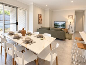 A modern living room with a dining area, a sofa set, a TV, and a floor lamp. - Slow Days on Wellington | A Family Retreat (Yarrabilba)