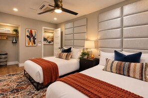 A hotel room with two beds, a ceiling fan, a nightstand with a lamp, and a large window.