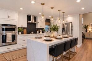 A modern kitchen with white cabinetry, stainless steel appliances, a marble island, and pendant lighting.