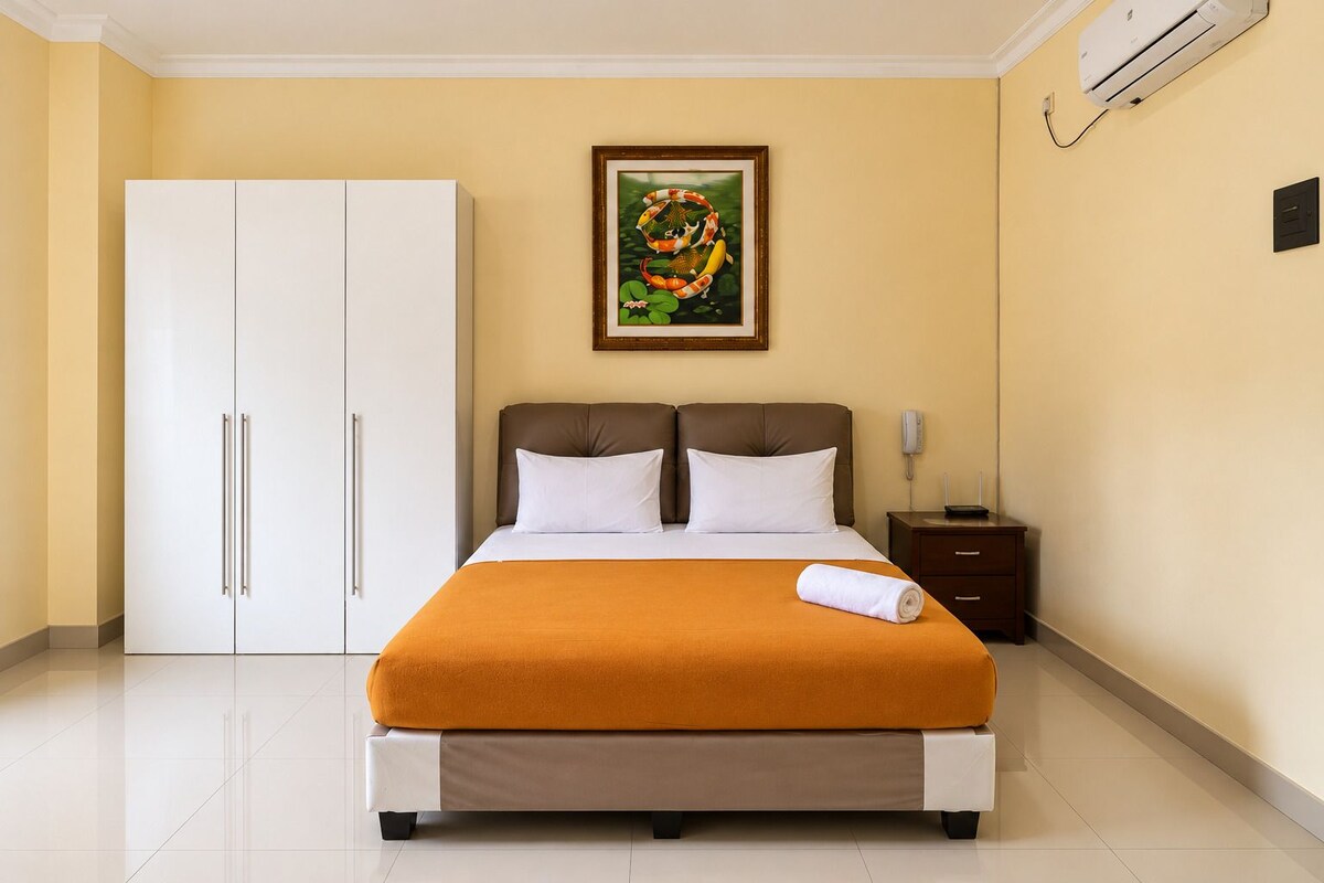 A hotel room with a bed, a wardrobe, a nightstand, a phone, and an air conditioning unit.