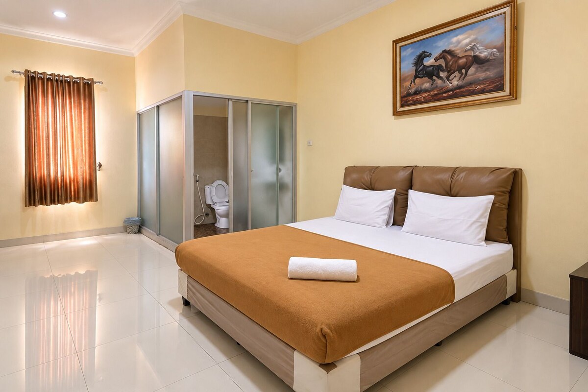 A hotel room with a large bed, a bathroom with a toilet and shower, and a painting on the wall.