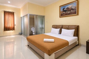 A hotel room with a large bed, a bathroom with a toilet and shower, and a painting on the wall. - Nice Room (Jakarta Pusat)