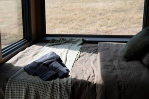 A bed with a view of a grassy field through a window.