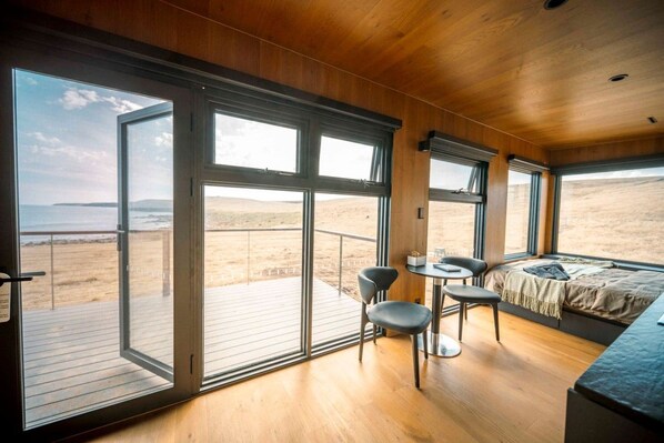 A room with large windows, a bed, a small table, and chairs.