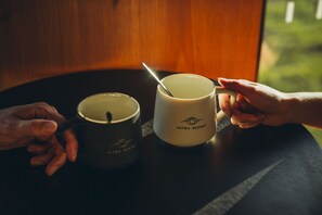 Two mugs on a table, one with a spoon in it, and a hand pointing at the mug.