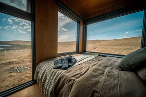A bedroom with a large bed, a view of a grassy landscape, and a window with a wooden frame.